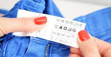 Eine Hand mit roten Nägeln hält ein Etikett mit Pflegehinweisen aus einem blauen Kleidungsstück Hintergrund unscharf Etikett zeigt verschiedene Pflege- und Waschsymbole