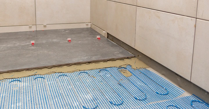 Das fachgerechte Verlegen von großformatigen Bodenfliesen auf einer elektrischen Fußbodenheizung. Der Fliesenkleber sorgt für eine optimale Wärmeleitung.