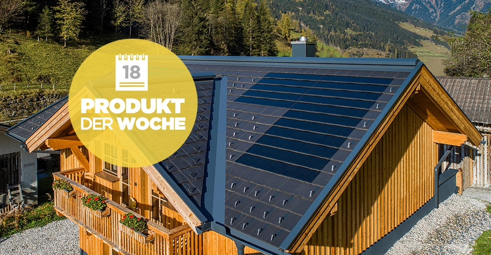 Ein Holzhaus mit Solarpaneelen auf dem Dach steht in einer bergigen Landschaft mit grünen Bäumen und schneebedeckten Bergen im Hintergrund. Text: 18 PRODUKT DER WOCHE