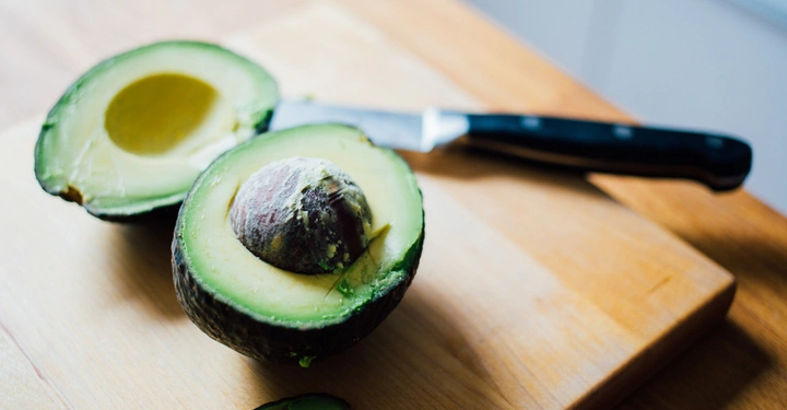Galerie-Bild 3: Eine halbierte Avocado liegt auf einem Holzbrett Messer daneben. In der Küche.