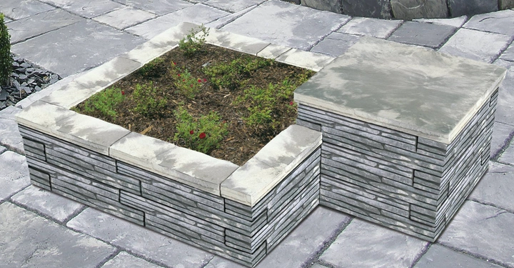 Galerie-Bild 7: Ein quadratisches Hochbeet aus grauen Ziegelsteinen, in dem kleine Pflanzen wachsen Umgebung aus grauen Steinfliesen. Daneben ein flacher, quadratischer Ziegelsteinblock als Sitzgelegenheit.