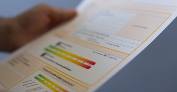 Hand hält Energieausweis mit deutlich erkennbarer Energieleiste von grün bis rot