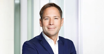 Lächelnder Dipl.Ing. Thomas Stini vor weißem Hintergrund in Anzug ohne Krawatte