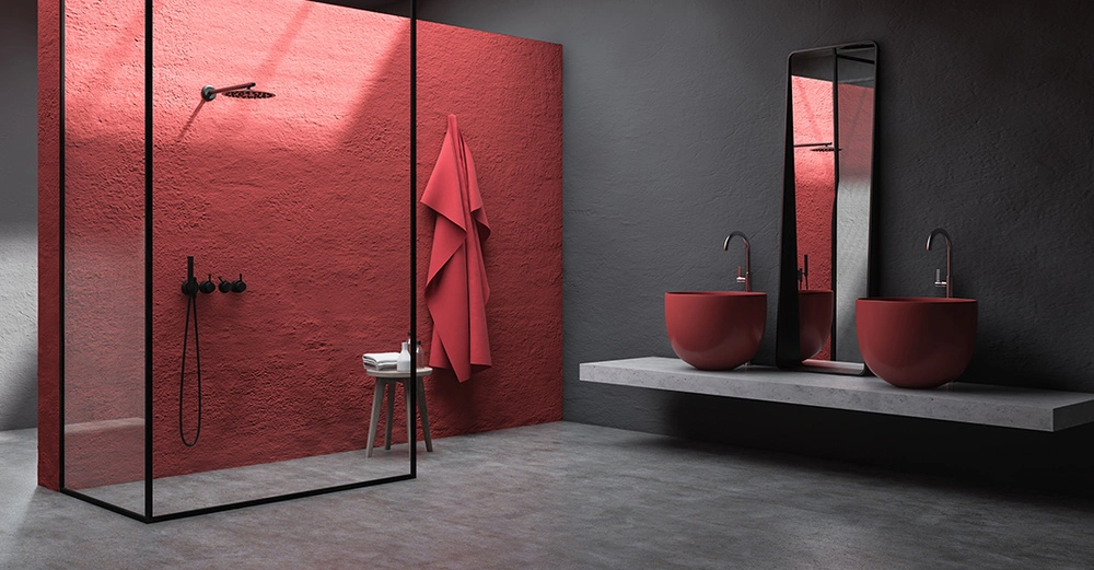 Dusche mit Glaswand und schwarzem Duschkopf an einer roten Wand links im modernen Badezimmer zwei rote Waschbecken und ein Spiegel auf grauer Ablagefläche rechts.