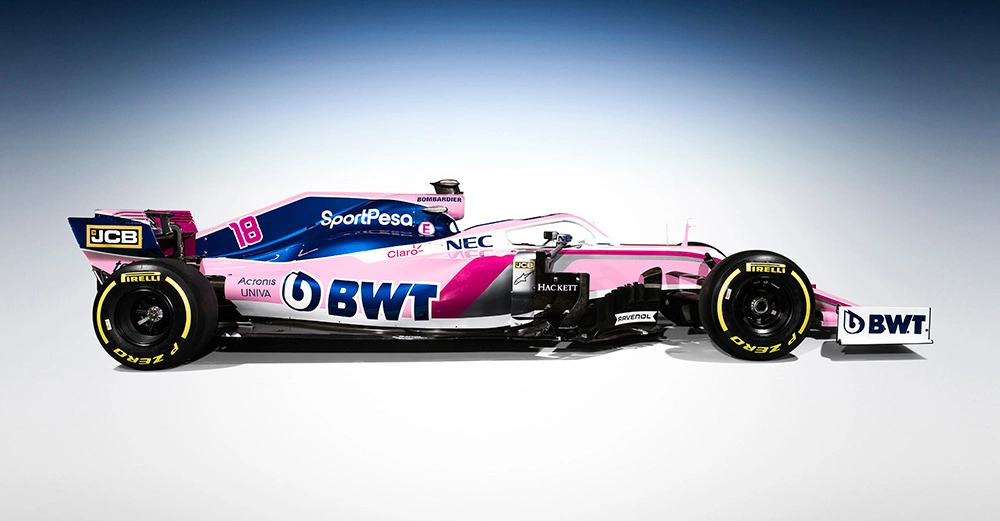 Ein Rennwagen in Rosa und Blau steht still in einem Studio. Auf dem Auto sind die Logos BWT SportPesa NEC JCB Acronis UNIVA Hackett Claro Pirelli und andere platziert.