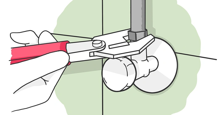 Eine Hand hält eine Zange, die ein Rohrventil greift; die Zange hat rote Griffe. Das Ventil ist an einer Wand befestigt.