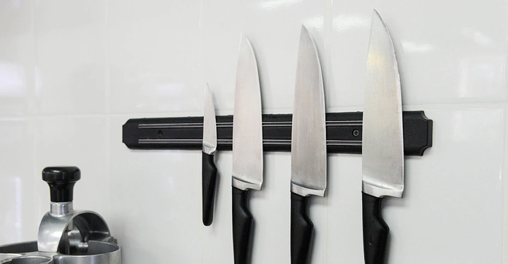 Schwarzer Magnetstreifen auf weißer Wand mit 3 großen Fleischmessern und 1 kleinen Gemüsemesser dran. 