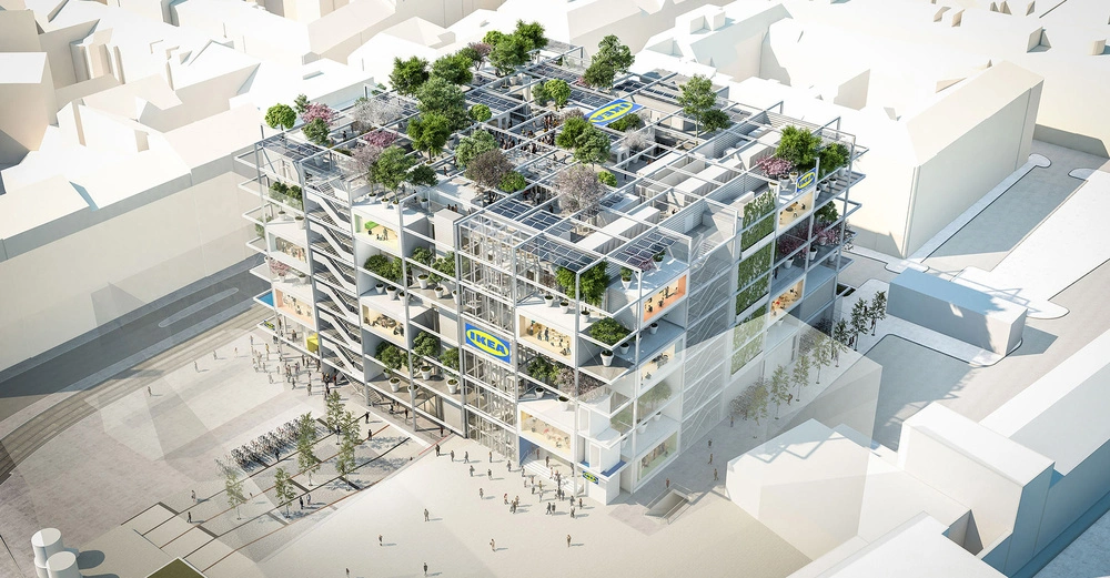 Ein mehrstöckiges Bauwerk mit zahlreichen Pflanzen auf dem Dach und den Etagen zeigt mehrere IKEA-Schilder im oberen Bereich der Fassade; umgeben von Stadtgebäuden und einer Fußgängerzone.