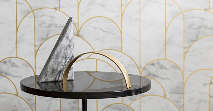Marmorpyramide steht auf rundem Tisch neben gebogenem goldenem Element im Raum mit weiß-goldener gemusterter Tapete