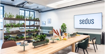 Ansicht des Sedus Showroom mit langem Holztisch und Pflanzenregalen
