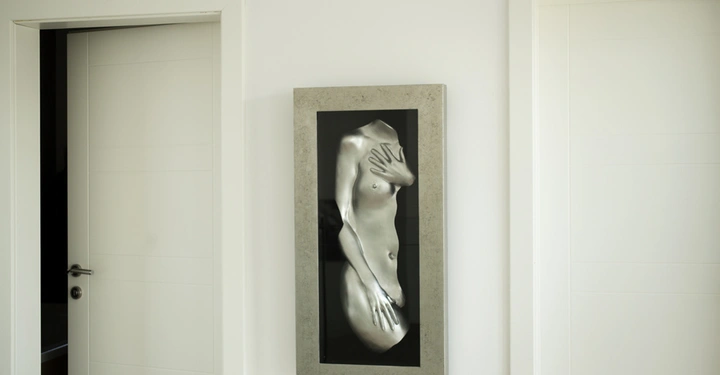 Galerie-Bild 2: Ein silbernes Relief einer nackten menschlichen Torsoskulptur mit erhobener Hand hängt zwischen zwei weißen Türen an einer weißen Wand in einem Innenraum.