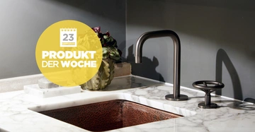 Ein Wasserhahn gießt auf eine Kupferspüle in einer Küche aus Marmor. Eine Pflanze steht daneben. Text auf gelbem Hintergrund: 23 PRODUKT DER WOCHE.