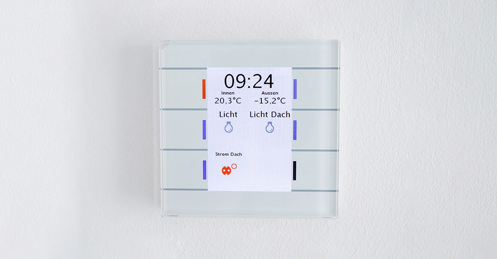 Digitaler Wandthermostat zeigt die Uhrzeit 09 24 und die Temperaturen Innen 20 3 Grad Celsius und Außen minus 15 2 Grad Celsius an Em Raumlichtsteuerung Bedienfläche umgeben von weißer Wand.