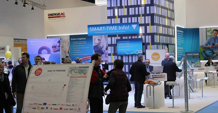 Galerie-Bild 10: Menschen stehen und gehen auf einer Messe vor Ständen mit Bannern und Schildern. Hauptbanner: SMART-TIME Info. Text: Halle 19/ENERGIE. Weitere Schilder: ENERGIE AG, ENERGY SAFE, Mehr Energie für mein Leben.