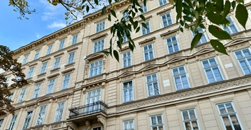 Wohnhaus im 1. Bezirk in Wien mit historischer Fassade, blauem Himmel und grünen Bäumen.