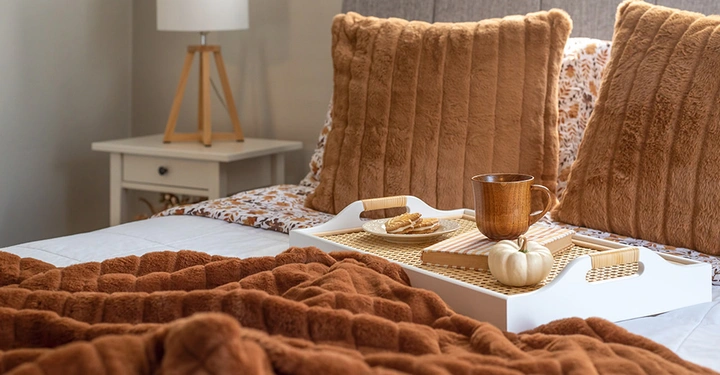 Ein Serviertablett mit einer Tasse, einem weißen Kürbis und Keksen stehen auf einem cozy Bett in Herbstfarben.