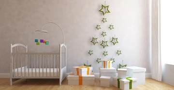Ein weißes Babybett steht in einem hellen Raum mit Holzboden, an der Wand sind grüne Sterne als Baumform aufgehängt, daneben mehrere Geschenke mit orangefarbenen und grünen Schleifen.