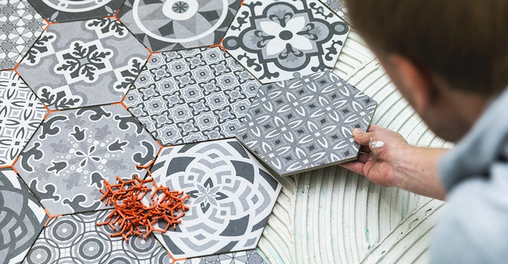 Ein Fliesenleger verlegt dekorative Hexagonfliesen in Zementfliesenoptik. Mit Fugenkreuzen wird ein exaktes Fliesenmuster für eine moderne Bodengestaltung erzielt.