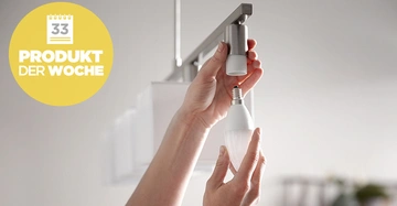 Hände schrauben eine Glühbirne in eine Deckenlampe ein Innenraum gelb-weißer Kreis mit Text Produkt der Woche Kalender Nummer 33