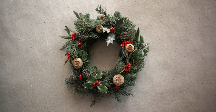 Weihnachtskranz aus grünen Zweigen und roten Beeren liegt dekorativ auf einem hellgrauen Betonboden.