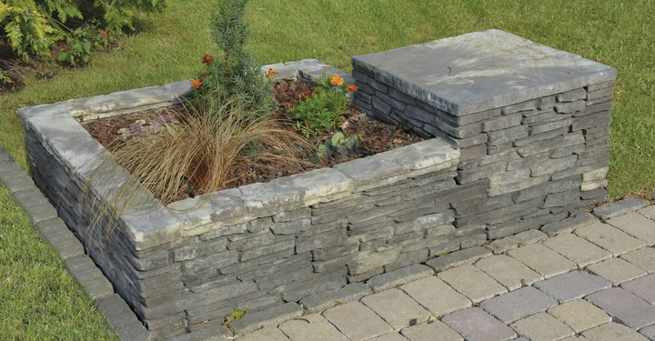 Galerie-Bild 8: Ein graues Steinbeet wächst bunte Blumen und Gräser auf einem gepflasterten Weg mitten im grünen Rasen in einem Garten.