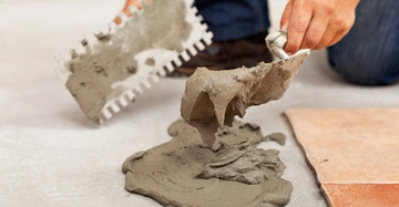 Hände verteilen Fliesenkleber mit einer Zahnkelle auf dem Boden bereiten so das Verlegen von Fliesen im Hintergrund vor.