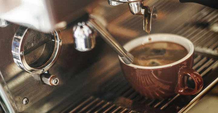 Kaffeetasse sammelt Kaffee während der Zubereitung aus einer glänzenden Espressomaschine in einer Kaffeebar.