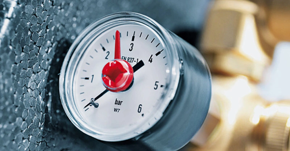 Druckmessgerät zeigt etwa 3 bar an in einer metallischen Umgebung montiert links schwarzes Styropor rechts goldene metallische Rohrleitungen Text EN 837-1 und bar W7