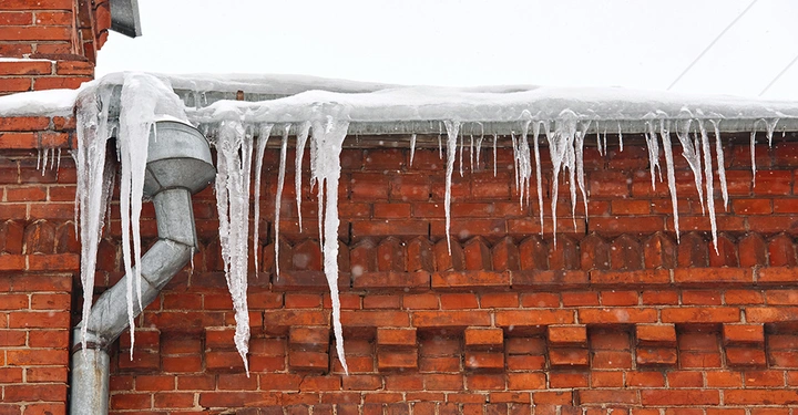 Vereiste Regenrinne mit Eiszapfen an einem Backsteinhaus, ein Risiko für die Dachentwässerung im Winter.
