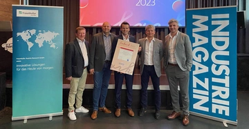 Fünf Männer posieren lächelnd im Anzug und halten ein Zertifikat in einem Konferenzraum mit Werbebannern von Fraunhofer Austria Research GmbH und INDUSTRIE MAGAZIN Text auf dem Zertifikat: Fabrik 2023 Green Factory