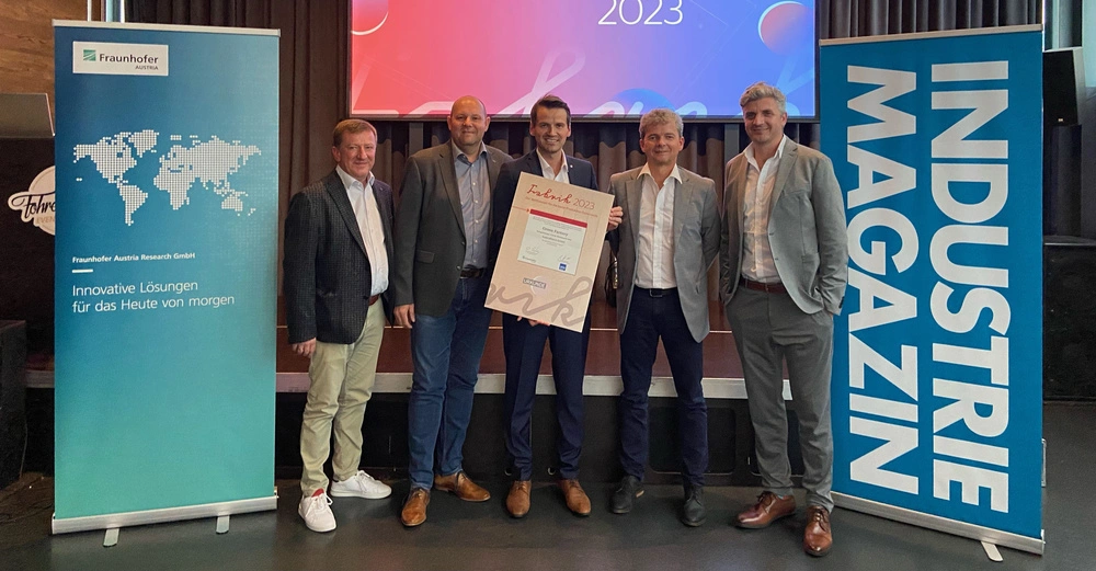 Fünf Männer posieren lächelnd im Anzug und halten ein Zertifikat in einem Konferenzraum mit Werbebannern von Fraunhofer Austria Research GmbH und INDUSTRIE MAGAZIN Text auf dem Zertifikat: Fabrik 2023 Green Factory