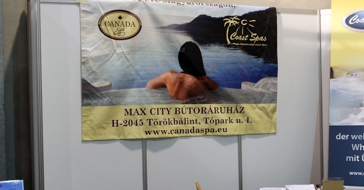 Galerie-Bild 22: Ein Poster zeigt eine Person in einem Whirlpool mit Blick auf den See im Hintergrund CANADA Spa Coast Spas MAX CITY BÚTORÁRUHÁZ H-2045 Törökbálint Tópark u 1 www.canadaspa.eu