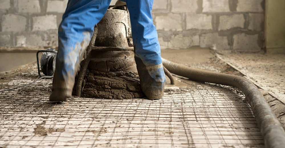 Mann in blauer Arbeitshose steht auf Estrichbewehrung und bringt mit Estrichpumpe das Material auf