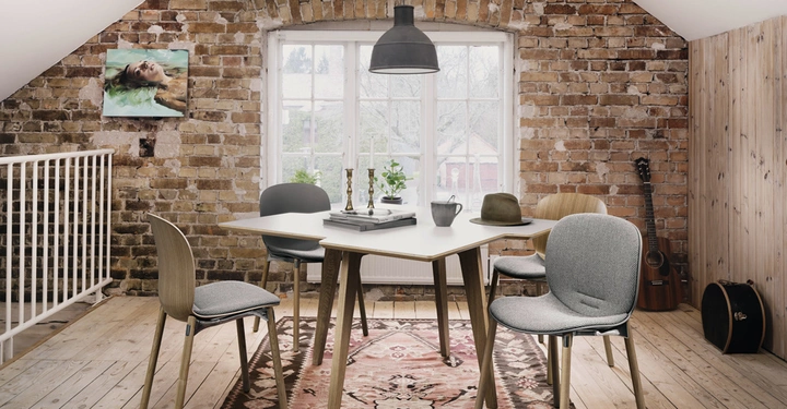 Ein Tisch mit Stühlen steht in einem gemütlichen Raum mit gemauerter Ziegelwand Holzboden und einem Fenster im Hintergrund Gitarren an der Wand und Bild an der Wand.
