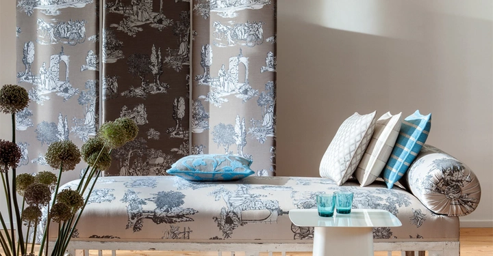 Galerie-Bild 3: Sofa mit gemusterten Kissen steht in einem modern eingerichteten Raum; im Vordergrund dekorative Pflanzen; im Hintergrund gemusterte Vorhänge und eine weiße Wand. Ein kleiner Tisch mit zwei Gläsern daneben.