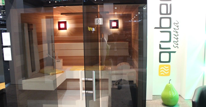 Galerie-Bild 13: Eine Sauna steht in einem Ausstellungsraum mit Glastür und Holzbänken. Leuchtende Schilder sind an den Wänden angebracht. Text: gruber sauna home spa.