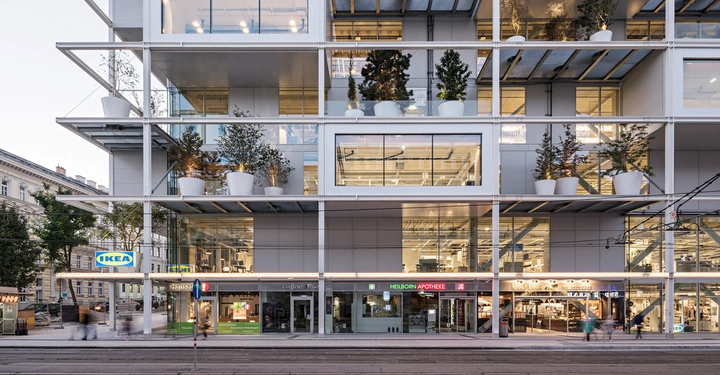 Galerie-Bild 2: Ein modernes Gebäude mit großen Glasflächen und Pflanzen in weißen Töpfen auf Balkonen mehrere Stockwerke hoch darunter Geschäfte wie IKEA Heilborn Apotheke Coiffeur Stefan im urbanen Stadtumfeld