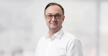 Alen Music, neuer Geschäftsführer von immOH! steht mit weißem Hemd und freundlich lächelnd vor weißem Hintergrund.