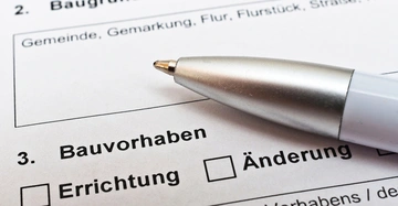 Formular für Baubewilligung liegt auf Tisch, Kugelschreiber darauf. Zu lesen: Bauvorhaben, Errichtung, Änderung
