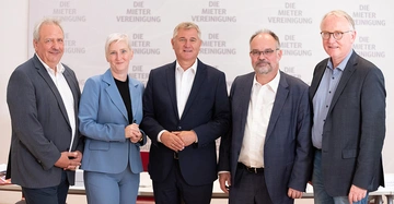 4 Männer in Anzug udn eine Frau im hellblauen Hosenanzug stehen lächelnd nebeneinander auf der Bühne der Pressekonferenz