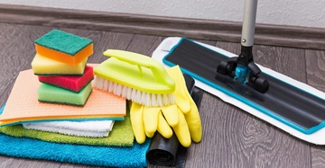 Dunkler Laminatboden mit einem Wischmopp neben einem bunten Haufen aus Wischtüchern und Putzschwämmen.