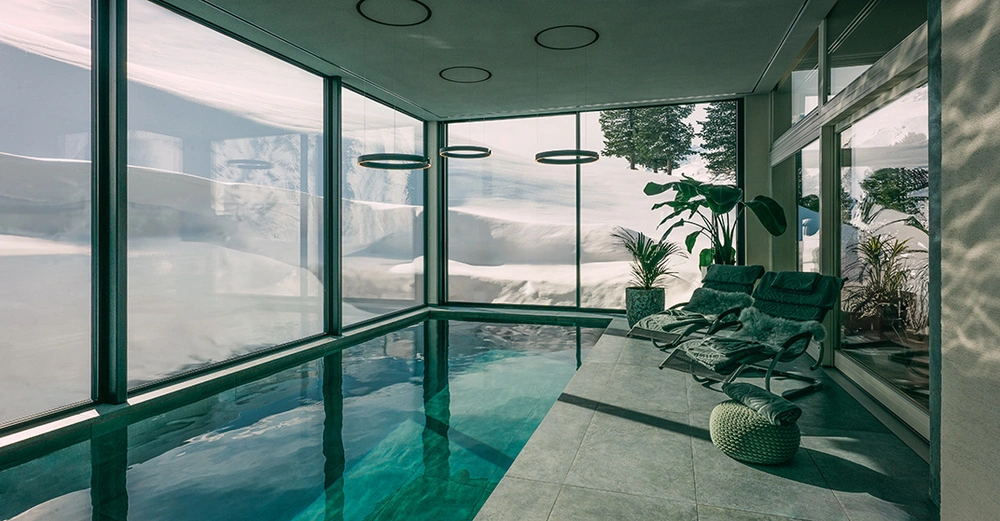 Türkises Naturpool im verglasen Innenbereich eines modernen Hauses mit Pflanzen und Beleuchtung