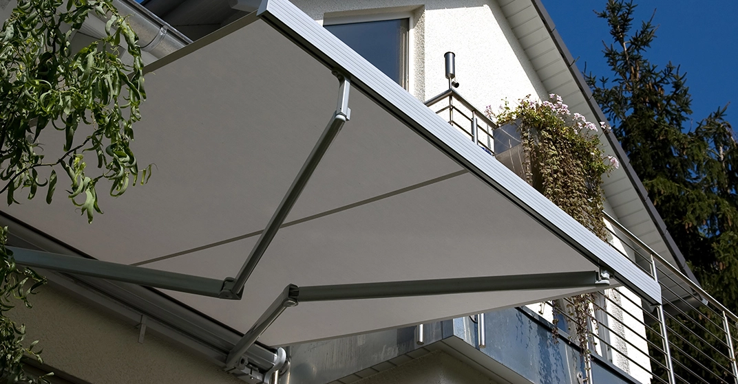 Ausfahrbare Markise spendet Schatten auf einem Balkon eines Einfamilienhauses an einem sonnigen Tag.