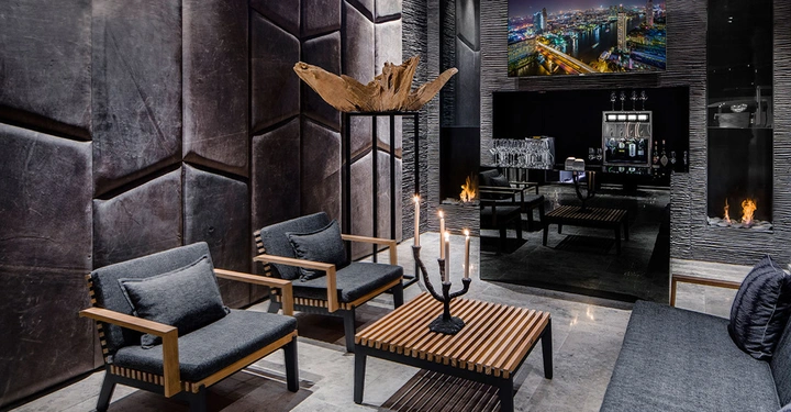 Moderne Wohnzimmermöbel mit Sofas und Sesseln aus Holz und grauem Stoff umgeben einen kleinen Tisch mit Kerzenleuchter vor einer Wand mit Kunstobjekt in einem luxuriösen Interieur mit Kamin und Stadtbild.