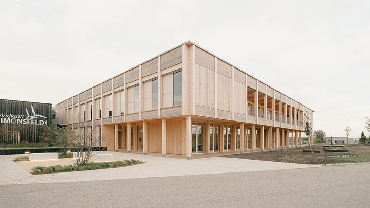 Galerie-Bild 3: Aufnahme eines großen zweistöckigen Holzbaus mit gepflastertem Vorplatz
