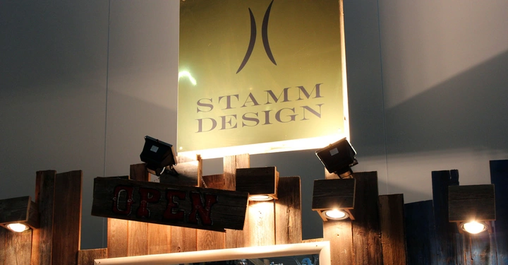 Galerie-Bild 5: Leuchtendes Schild mit Stamm Design im Fokus befestigt an einer rustikalen Holzwand im Innenbereich darunter ein Holzschild mit Open Text und ein beleuchtetes Fenster mit humorvoller Aufschrift Text STAMM DESIGN OPEN MEN WITH NO SHIRT NO SERVICE LADIES WITH NO SHIRT FREE DRINKS