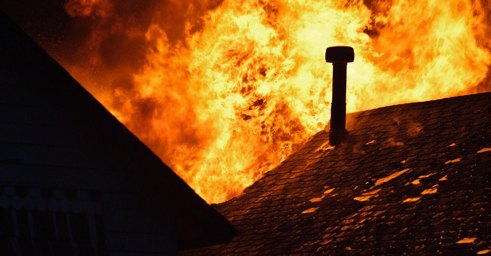 Flammen brennen auf dem Dach eines Gebäudes in der Nacht, umgeben von anderen Gebäuden im Dunkeln