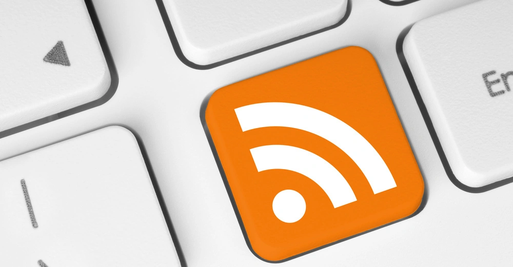 Orange Taste mit RSS-Feed-Symbol auf einer weißen Computertastatur in Nahaufnahme zeigt den Kontrast zwischen der markanten farbigen Taste und den standardmäßig weißen Tasten.