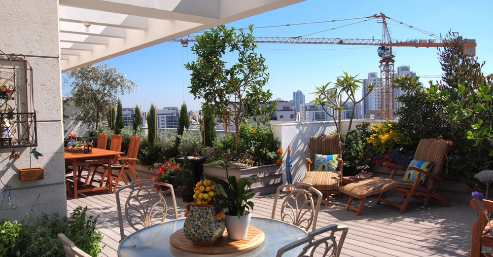 Eine dekorierte, sonnenbeschienene Dachterrasse auf einem Haus in der Großstadt mit Liegestühlen, Pflanzen und Sitzgelegenheiten.