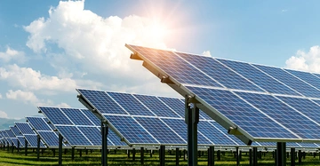 Reihen von Solarmodulen auf einer grünen Wiese unter blauem Himmel mit Sonnenschein, die die von der ASFINAG zur Verfügung gestellten Flächen für Photovoltaikprojekte durch Dritte symbolisieren und zur Energiewende in Österreich beitragen.